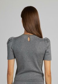 Szary dzianinowy top z krótkimi rękawami, bufkowymi ramionami i detalem w kształcie dziurki z tyłu, z subtelnym połyskiem. Gładka tekstura o dopasowanym kroju.