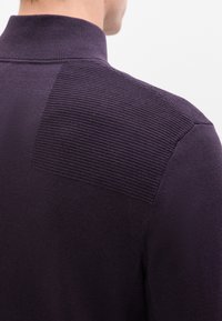 Tmavě fialový svetr s vysokým límcem, který má texturovanou část na horní části zad. Hladká pletená textura po celém svetr.