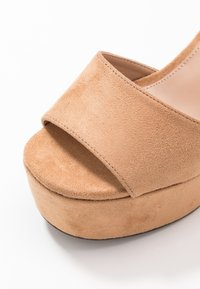 Tan zamšové platformové sandály s širokým páskem přes nohu a texturovaným povrchem, zaoblenou špičkou a silnou podrážkou.