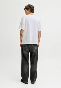 Camiseta blanca de algodón con mangas cortas y escote redondo, combinada con unos vaqueros negro holgados de mezclilla con textura deslavada y bolsillos traseros.