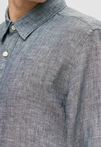 Ärmlös skjorta i texturerat mörkgrått linne med krage som knäpps, prydd med vita knappar och ett subtilt, vävt mönster.