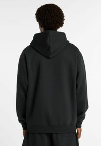 Haut à capuche noir en tissu doux, doté d'une grande capuche, d'une coupe décontractée et de poignets côtelés. Design minimaliste sans logos visibles.