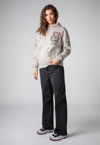 Grijze hoodie met kleurrijke grafische ontwerpen, gecombineerd met zwarte wide-leg jeans en witte sneakers met zwarte accenten en gumzolen.