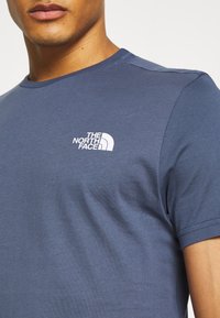 Námořnická modrá tričko s krátkým rukávem z hladkého materiálu; má bílé logo na levém prsu. Klasický design s kulatým výstřihem.