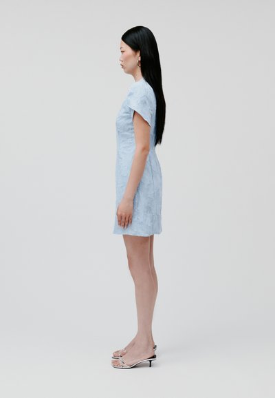 Hellblaues Kleid mit einem strukturierten Blumenmuster, taillierte Silhouette, kurze Ärmel und in Kombination mit schwarzen Absatzsandalen. Glattes Material.