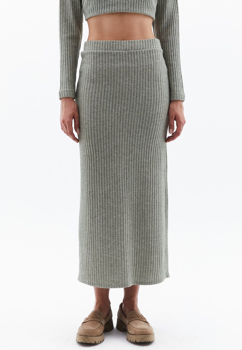 Jupe midi en tricot côtelé gris avec une taille ajustée et une fente sur le côté, associée à des mocassins marron clair. Texture douce et matériau extensible.