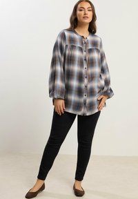 Pitkähiha, nappikiinnitteinen ruudullinen paita sinisen, ruskean ja valkoisen sävyissä; säännölliset hihat ja löysä malli. Mustat kapeat farkut ja ruskeat tasapohjaiset kengät.