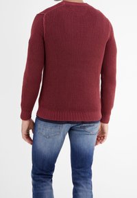 Bordeauxfärgad stickad tröja med ett strukturerat mönster, ribbad ärmslut och nederkant samt rund halsringning, bärs över blå denimjeans.