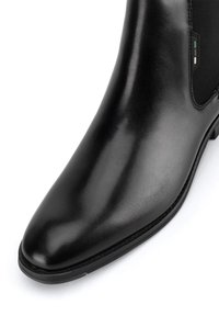 Bota de tobillo de cuero negro con un diseño elegante, punta afilada, paneles laterales elásticos y detalle de costura en color contrastante en la suela.