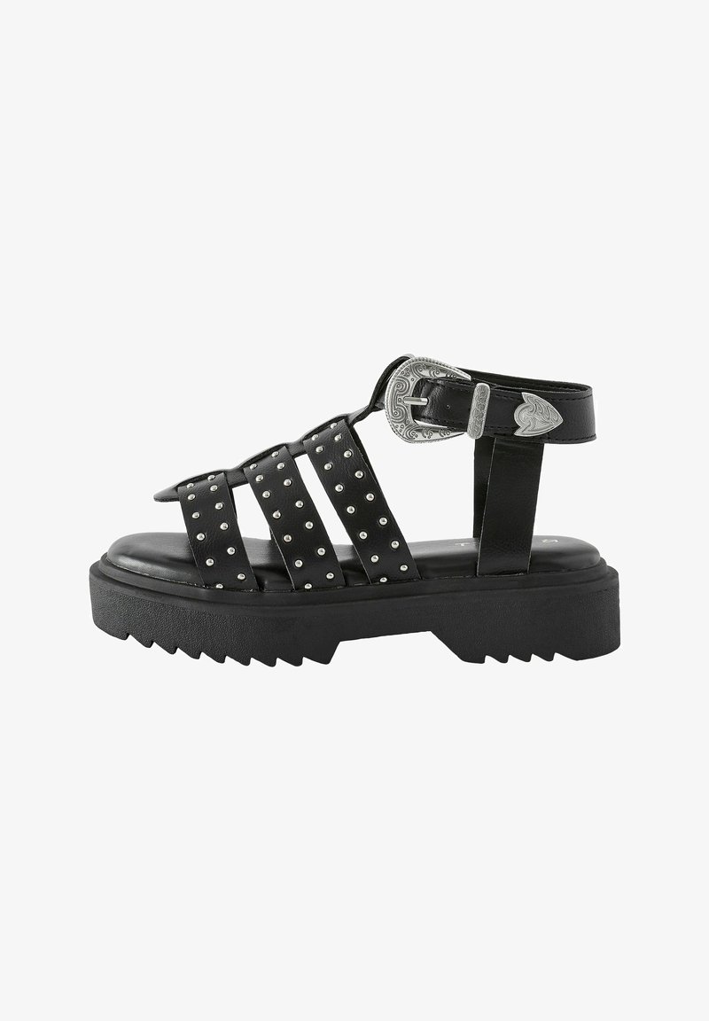 Sandal en cuir noir avec des sangles cloutées, une semelle épaisse et une boucle décorative en argent. Dispose d'un fond strié pour une meilleure adhérence.