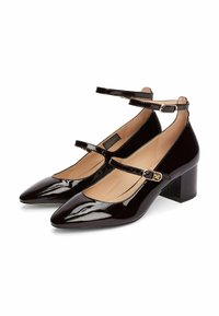 Tacones de charol burdeos con punta afilada, correas en el tobillo y tacones de bloque. Textura suave con un acabado brillante y detalle de hebilla de metal.