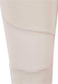 Leggings beige clair avec une texture lisse, comportant un panneau en mesh sur la partie médiane et des détails de couture subtils pour ajouter des éléments de design.