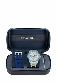 Conjunto de reloj Nautica en un estuche con cremallera, que presenta un reloj de acero inoxidable con acentos azules, una correa de silicona azul y una herramienta para ajustes.
