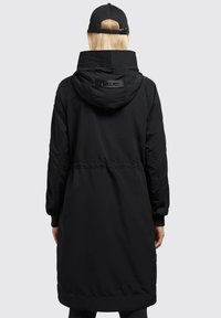 Černá nepromokavá parka s kapucí, stahovaným pasem, elastickými manžetami a logem na zadní straně. Dlouhý a rovný silueta. Hladká textura.