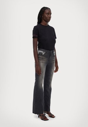 Black fitted t-shirt with colorful striped accents on sleeves, paired with flared denim jeans featuring embroidered front pockets and light fading.