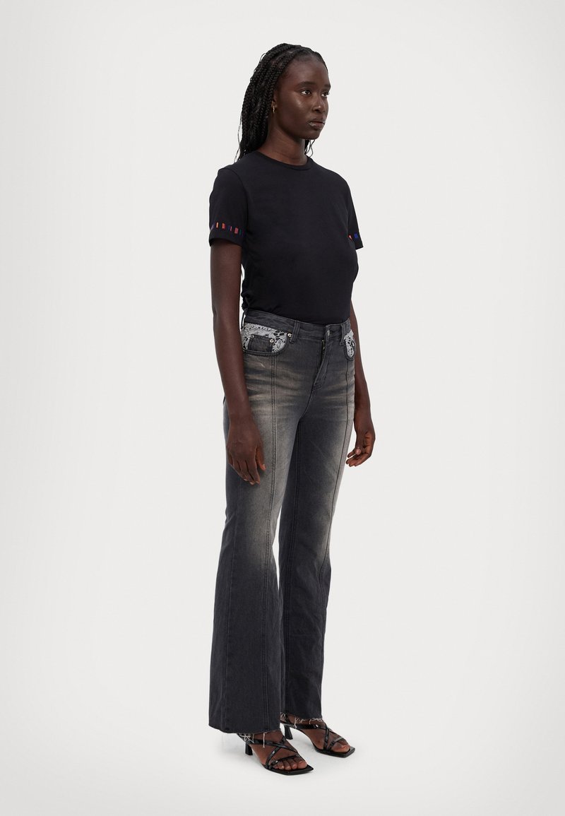 Svart åtsittande t-shirt med färgglada randiga detaljer på ärmarna, kombinerad med utsvängda denimjeans som har broderade framfickor och lätt blekning.