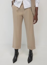 Beige maßgeschneiderte Hose mit geradem Bein, gekrempeltem Saum und Seitentaschen, kombiniert mit eleganten schwarzen spitzen Stiefeletten.