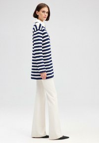 Navy és fehér csíkos hosszú pulóver, galléros nyakkal, slim-fit fazonban, krémszínű, bő szárú nadrággal és fekete laposcipővel viselve.