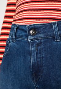 Ribbade röda, orangea och svarta randiga skjortan som bärs med blå denimjeans med framsida knäppning och klassisk fem-fickorsdesign.