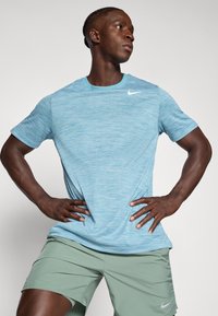 Lyseblå kortermet treningsskjorte med teksturert mønster. Har en liten hvit Nike-logo ved kragen. Brukt med grønne shorts.