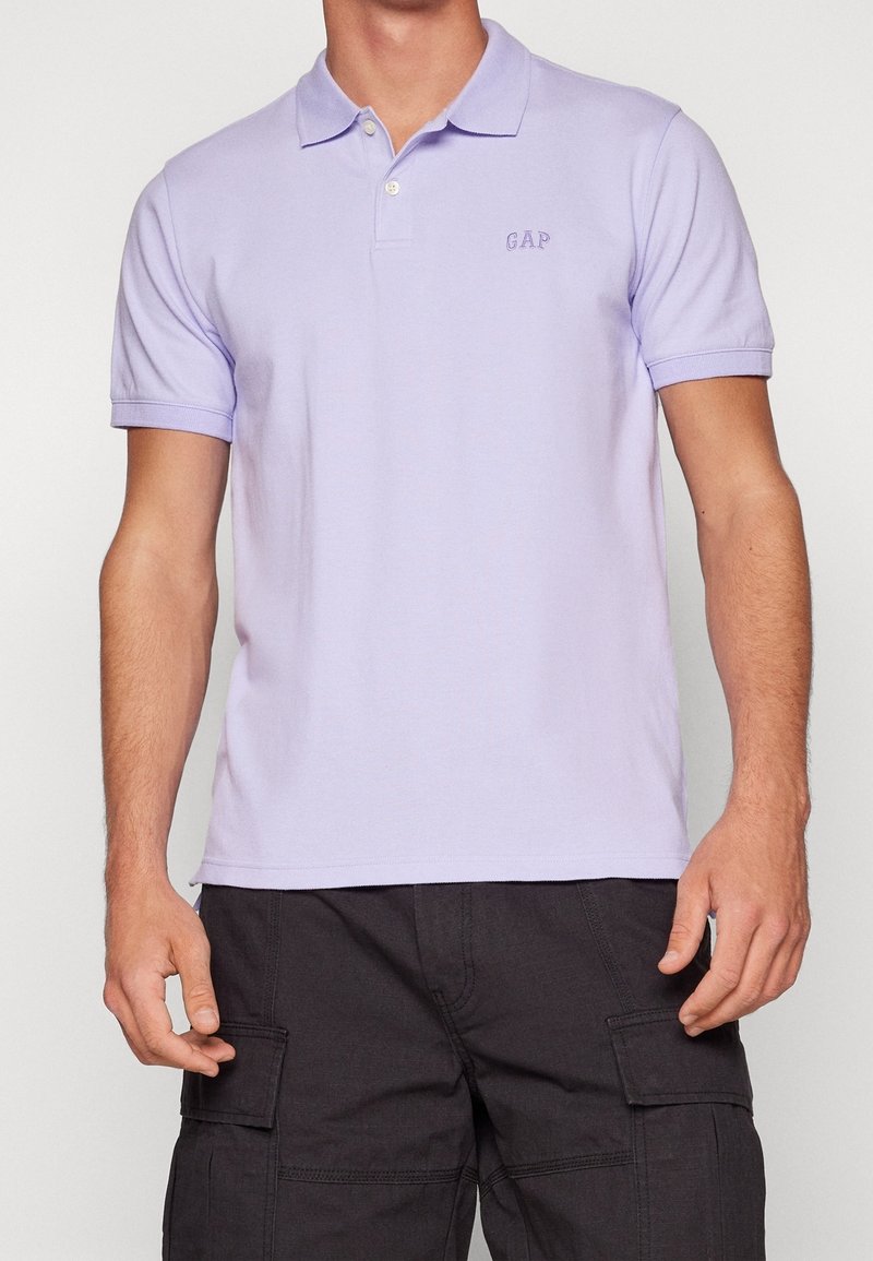 Polo en coton lilas avec col, patte de boutonnage à deux boutons et logo brodé "GAP" sur la poitrine. Manches courtes et coupe ajustée.