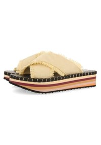 Mules tissés jaunes avec des bords effilochés, dotés d'une semelle compensée rayée multicolore et d'une semelle extérieure en caoutchouc noir cannelé.