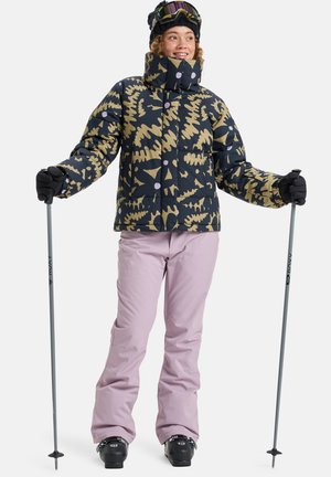 Gestepptes Skijacke in Marineblau mit beigem abstraktem Muster, ergänzt durch pastelrosa Schneehosen. Schwarze Handschuhe und Skistöcke runden den Look ab.
