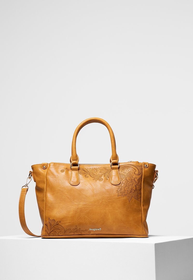 Sac à main en cuir marron clair avec embossage floral, deux poignées et une bandoulière amovible sur un socle blanc.
