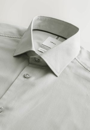 Cămașă de damă cu nasturi, de culoare gri deschis, cu textură, cu guler evazat, prezentând doi nasturi și o etichetă de brand parțial vizibilă pe interiorul gulerului.