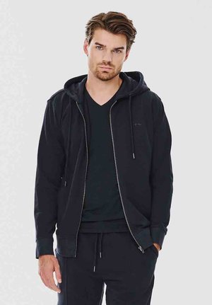 Czarna rozpinana bluza wykonana z miękkiej tkaniny, z kapturem na sznurki, kieszeniami po bokach i dopasowanym krojem, zestawiona z czarną koszulką.