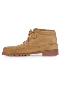 Botas cortas de ante en color beige con punta redonda, cierre con cordones y suela de goma gruesa que presenta un patrón de relieve pronunciado.