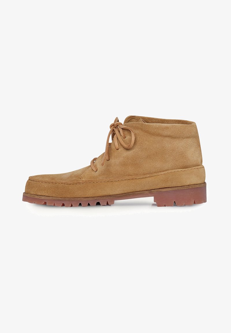Botas cortas de ante en color beige con punta redonda, cierre con cordones y suela de goma gruesa que presenta un patrón de relieve pronunciado.
