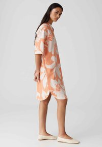 Perzik gekleed met een wit bloemenpatroon, losse pasvorm, ronde halslijn, mouwen van gemiddelde lengte en zijsplitten aan de zoom, gecombineerd met beige flats.