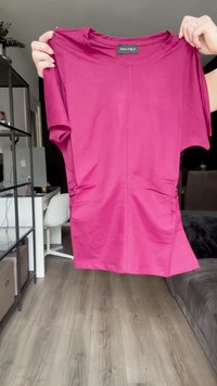 Top fucsia a maniche corte con scollatura rotonda, dettagli arricciati sui fianchi e un tessuto morbido e elasticizzato. Etichetta del marchio visibile sul collo.