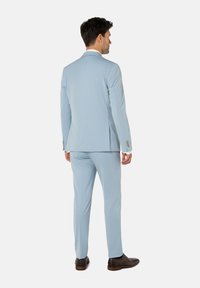 Veste de costume bleu clair et pantalons, tissu texturé, design simple, deux fentes arrière, chaussures marron, vue de dos.