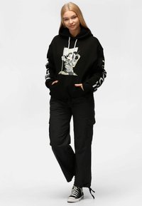Felpa nera con cappuccio e stampa grafica che raffigura un topo astronauta, abbinata a pantaloni cargo neri e sneakers nere. Presenta lacci e tasche.