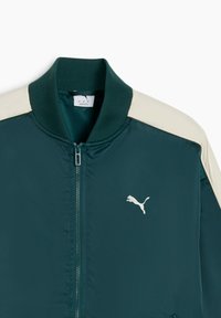 Donkergroene bomberjack met crèmekleurige schouderaccenten, geribbelde kraag, ritssluiting en een klein wit logo op de borst. Slank, nylon materiaal.