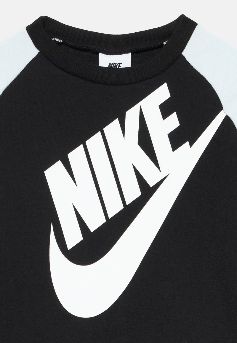Maglietta nera a maniche corte con un grande logo bianco "Nike" e grafica swoosh, con dettagli azzurri sulle spalle.