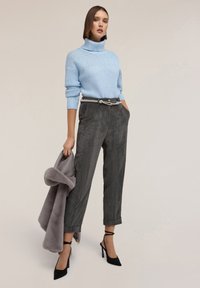 Ljusblå stickad tröja med hög krage, i kombination med mörkgrå manchesterbyxor. Modellen håller en grå fuskpälsjacka och bär svarta klackar.