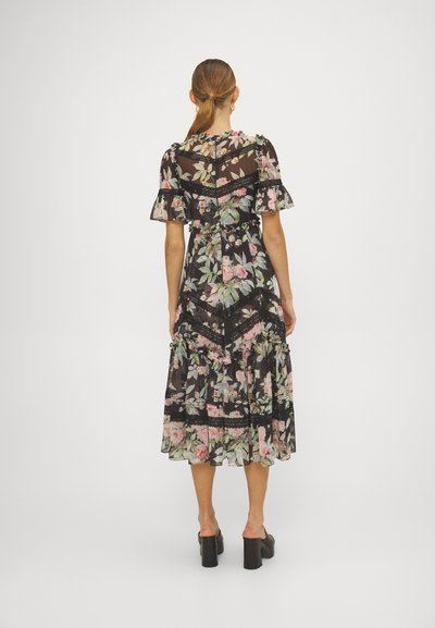 Bloemige maxi-jurk van zwart doorschijnend materiaal, met roze en groene patronen, ruches aan de mouwen en kant accenten, in een getailleerde silhoutte.