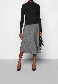 Černý žebrovaný rolák v kombinaci se šedou kostkovanou midi sukní. Outfit doplňují černé lodičky s špičatou špičkou a malá černá kabelka.