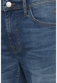 Jeans en denim bleu foncé avec une texture lisse, comportant des coutures jaunes, un bouton à l'avant et des poches sur les côtés.