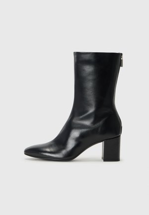 Bottine en cuir noir avec un bout pointu et un talon carré de 4 cm. Design élégant avec une fermeture éclair sur le côté pour un enfilage facile. Texture lisse.