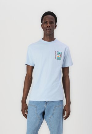 Camiseta de algodón de color azul claro con mangas cortas y cuello redondo. Presenta un gráfico colorido de una palmera en el bolsillo izquierdo del pecho.