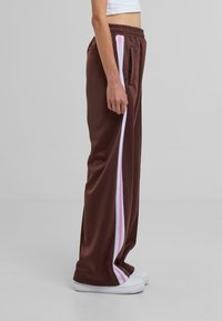 Pantalones deportivos marrones de corte relajado, con franjas laterales en rosa y blanco, una cinturilla elástica y un bolsillo con cremallera.