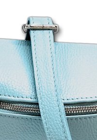 Detail einer hellblauen Lederhandtasche mit Reißverschluss, strukturiertem Oberflächenmaterial und glattem Tragegurt mit metallischen Hardware-Elementen.