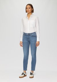 Witte overhemden met een borstzak, gecombineerd met blauwe skinny jeans en witte sneakers met zwarte accenten en een tan zool.