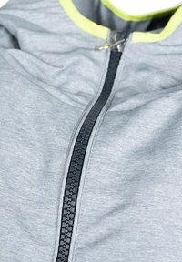 Grå zip-up jakke lavet af blødt materiale. Har en sort lynlås og en neon gul detalje langs kraven.