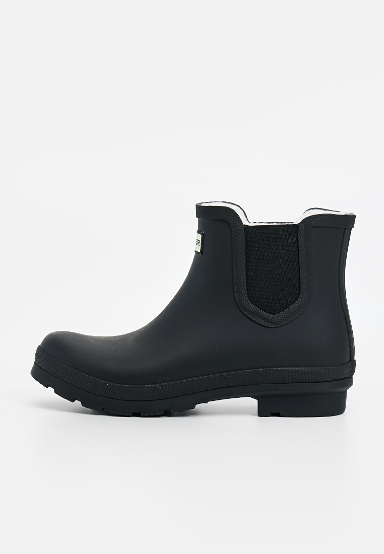 Schwarzer Gummistiefel mit elastischen Seitenpaneelen, abgerundeter Spitze, strukturiertem Sohle und einem kontrastierenden weißen Innenfutter.