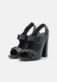Schwarze Leder-Absatzsandalen mit offenen Zehen, Schnallenakzenten und Slingback-Design. Sie verfügen über einen klobigen hohen Absatz und eine glatte Textur.